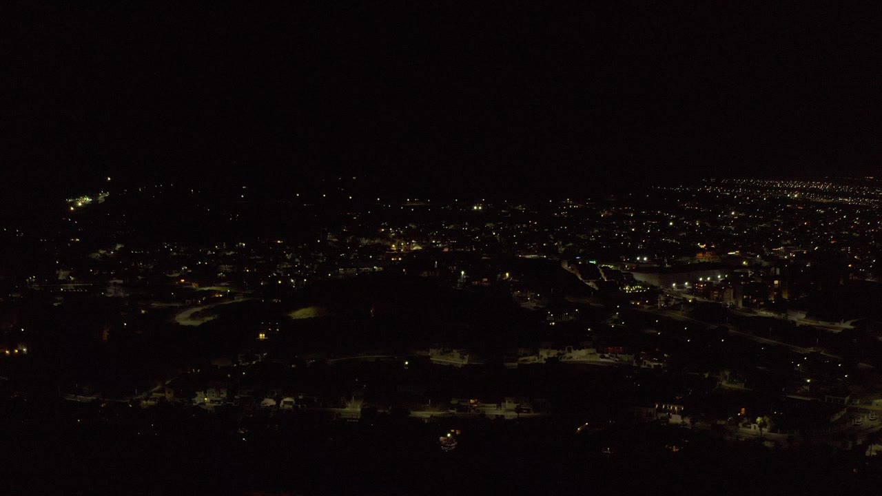 Opening frame of Los Cabos at night from above, with scattered streetlights, dark foreground land, distant town lights, and no visible people.