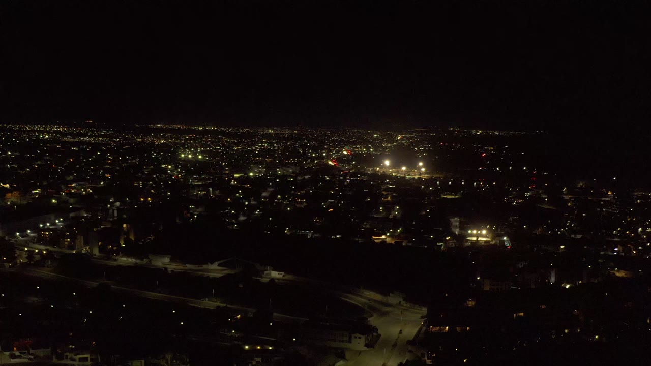 Los Cabos nighttime city view with a low horizon, scattered yellow-white lights, shadowed buildings below, and no visible people.