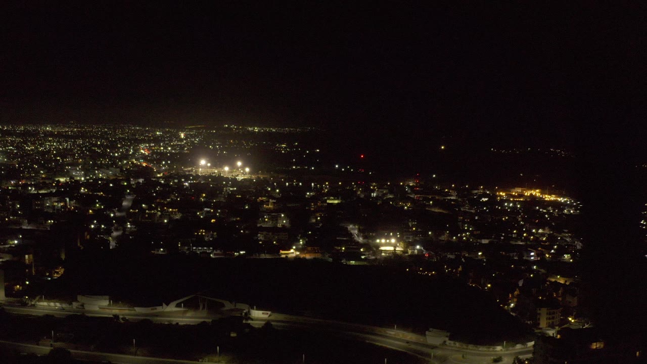 Los Cabos night view with bright urban light clusters across the midground, a dark foreground shoreline, and no visible people in the frame.