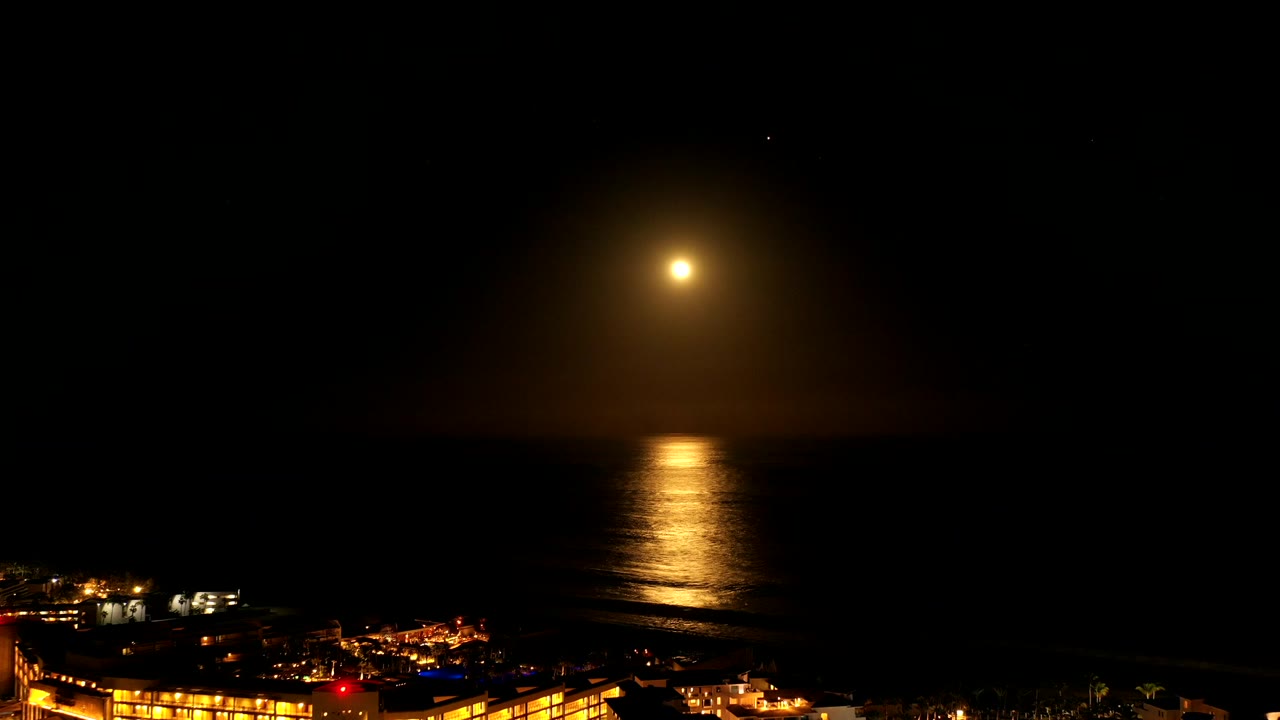 Warm light over a dark ocean with shoreline lights below.