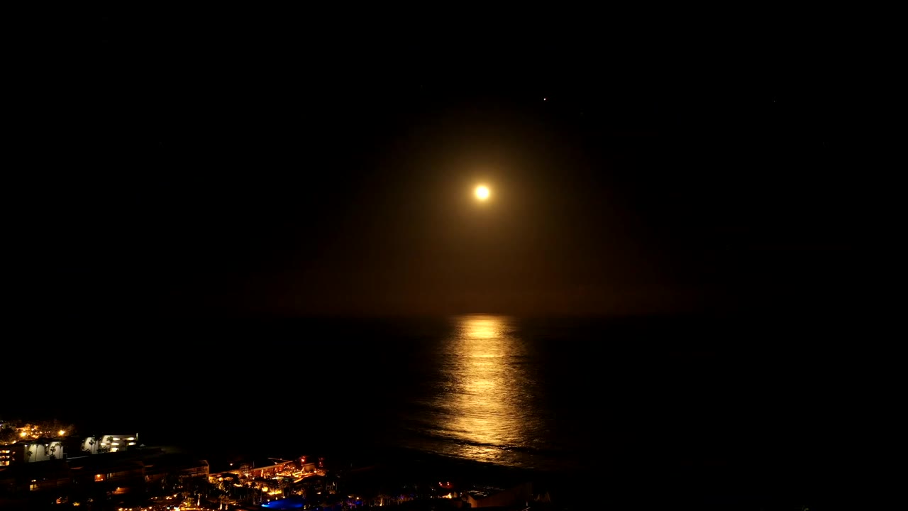 Golden reflection on ocean with faint coast lights near the bottom.