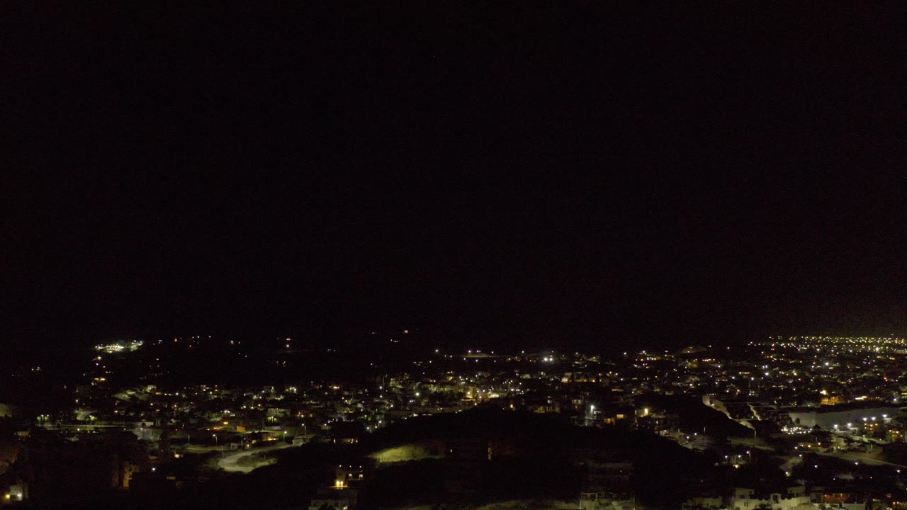 A later Los Cabos night frame holds the city lights near the lower third, with a black foreground shape and no visible people.