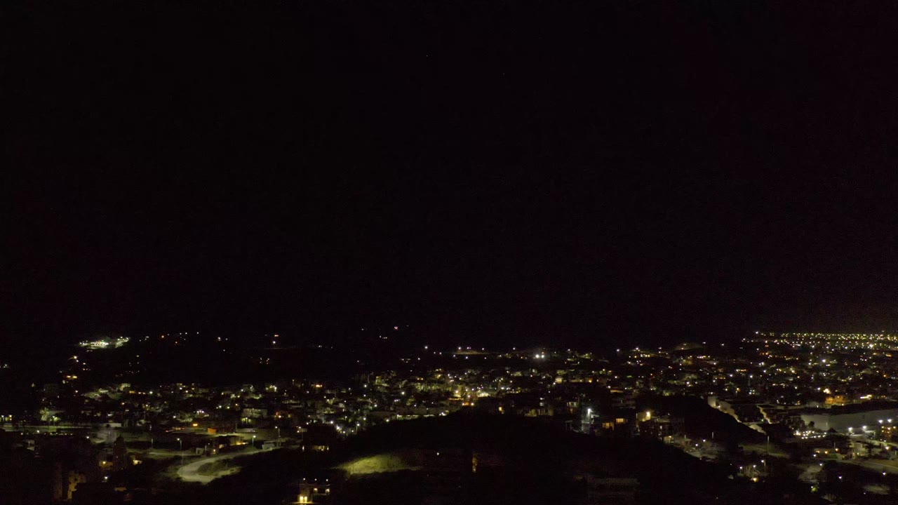 Los Cabos nighttime aerial with brighter road and building lights clustered toward the right side, dark foreground terrain, and no visible people.