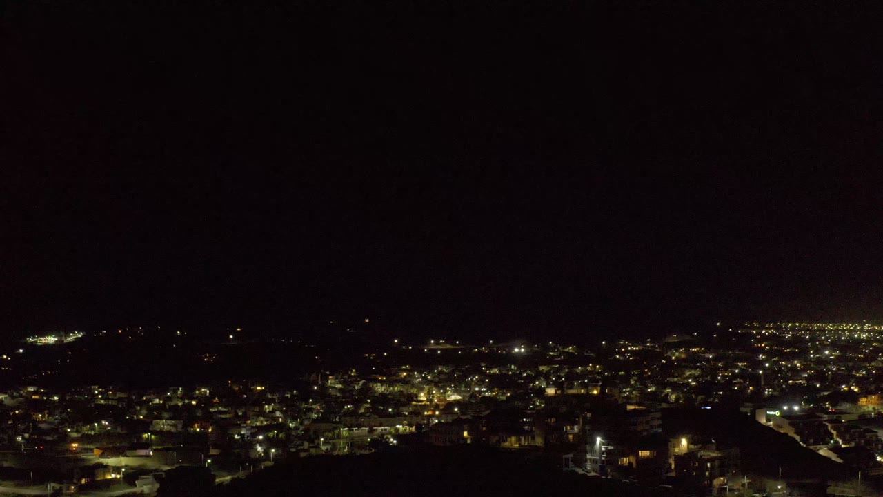 Los Cabos night scene with clustered yellow and white lights, a dark ridge line across the middle distance, and no visible people.