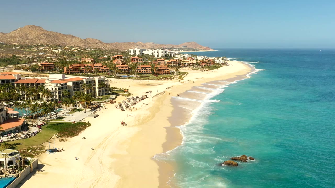 Aerial view of resort hotels beside a sandy beach and turquoise ocean.