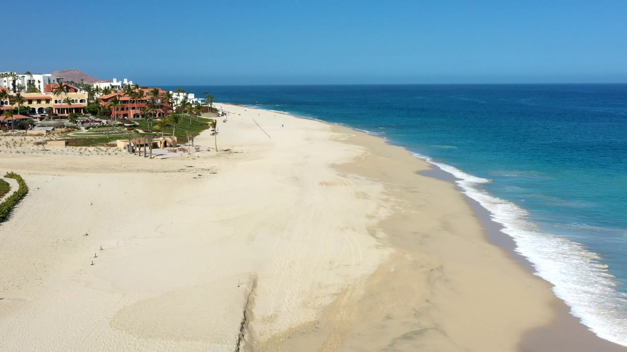 Aerial view of sandy beach, blue ocean, surf, and beachfront buildings.