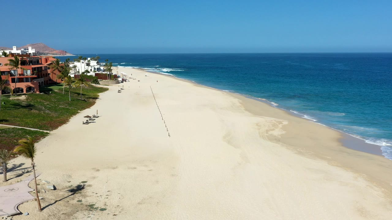Aerial view of a wide beach beside blue ocean and beachfront houses.