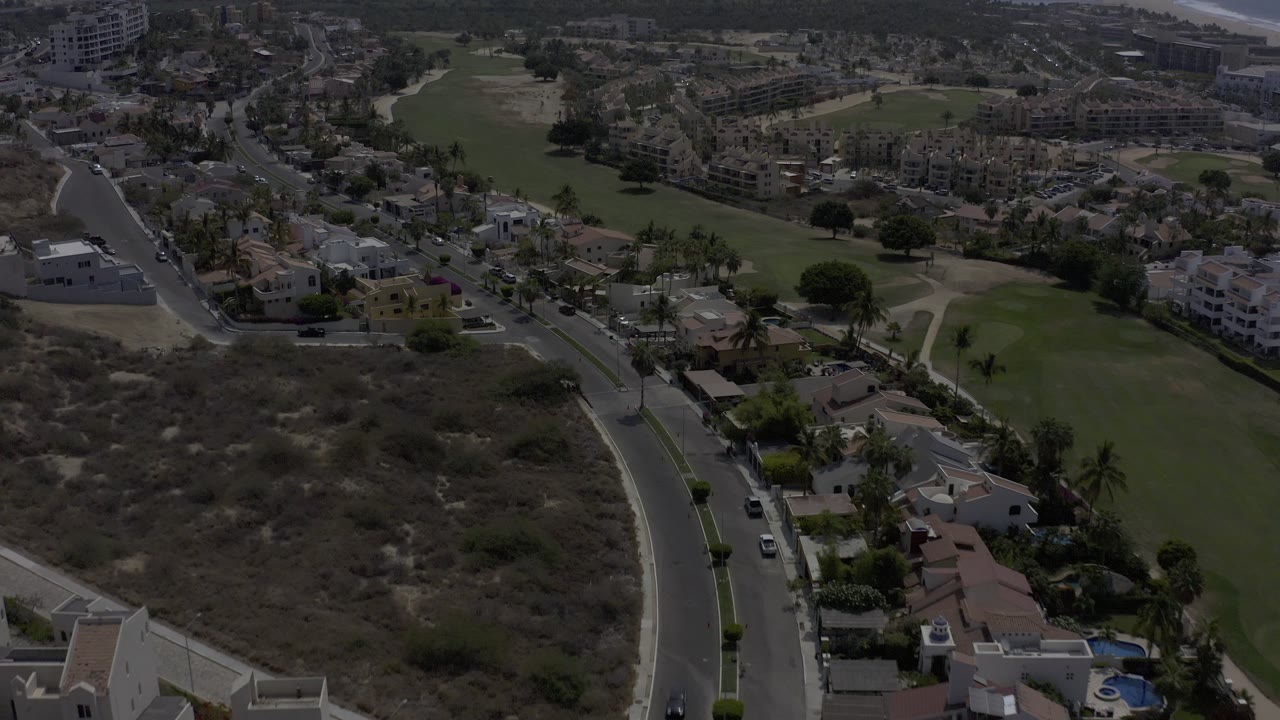 Top-angle view of a road beside scrubland, villas, and green fairway sections.