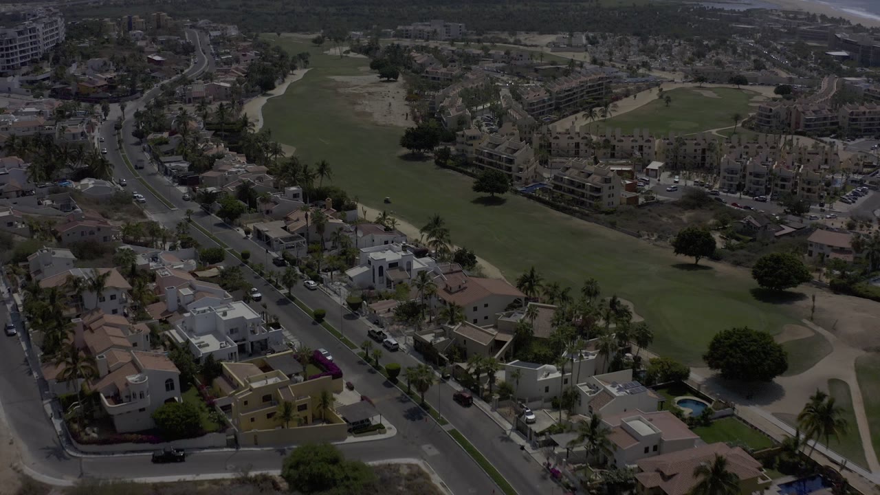Drone-like view of houses beside a large open green field.