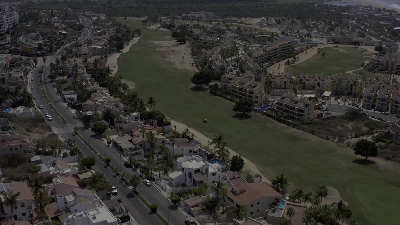 Aerial neighborhood view with a large grassy area, roads, homes, and buildings.