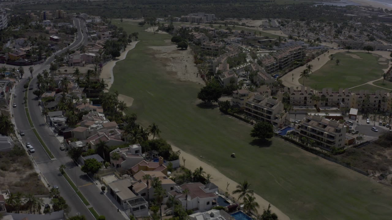 Aerial view of golf fairway, curved road, homes, and hotel buildings.