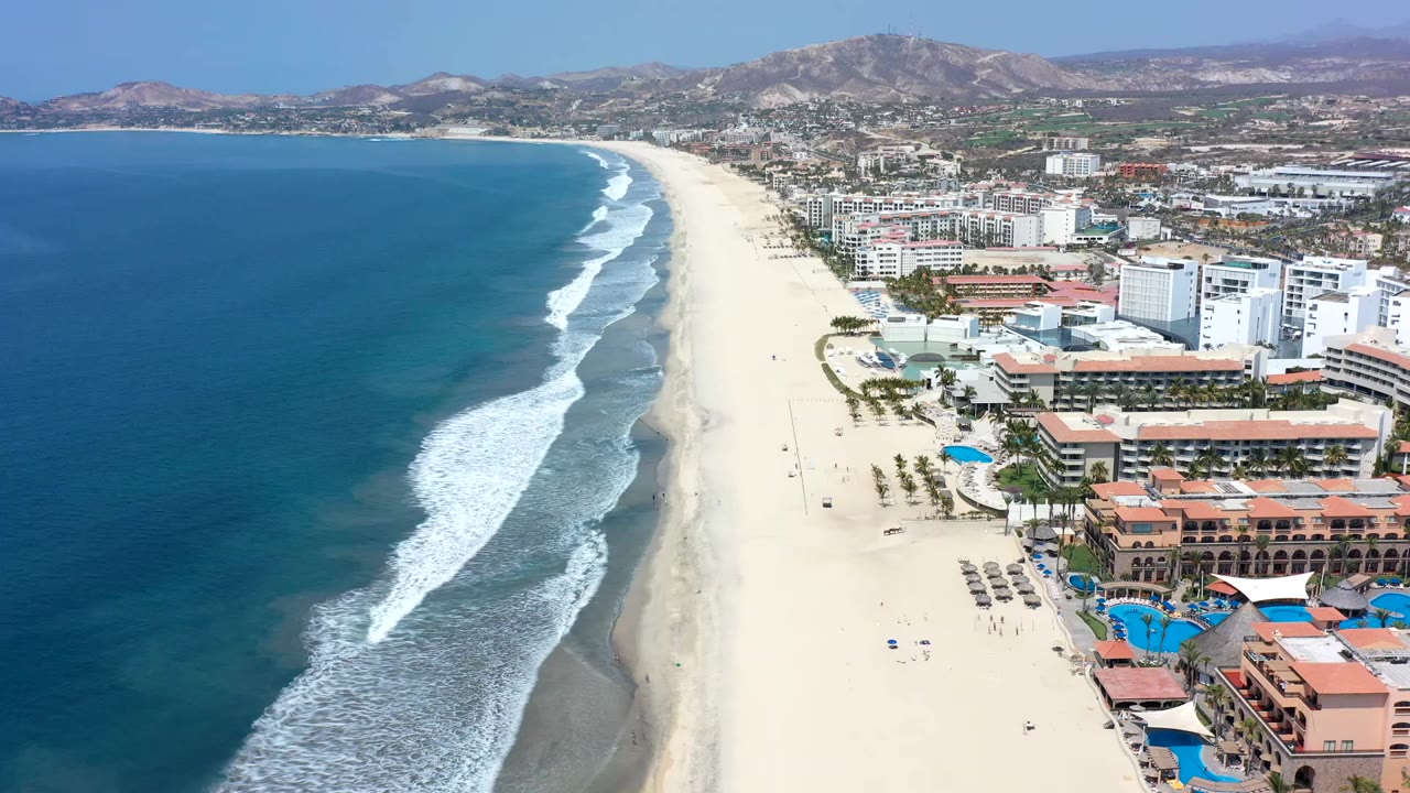 Aerial view of ocean waves beside a sandy resort beach.