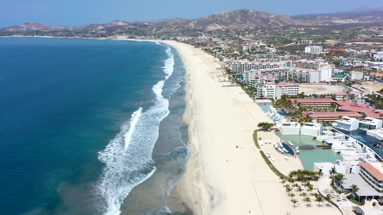 Aerial coastline with ocean, surf, beach, hotels, and hills.