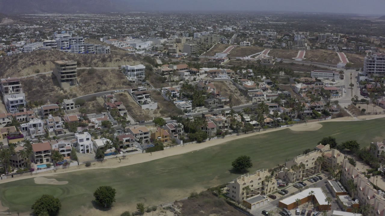 Aerial view of a green field beside hillside homes and roads.