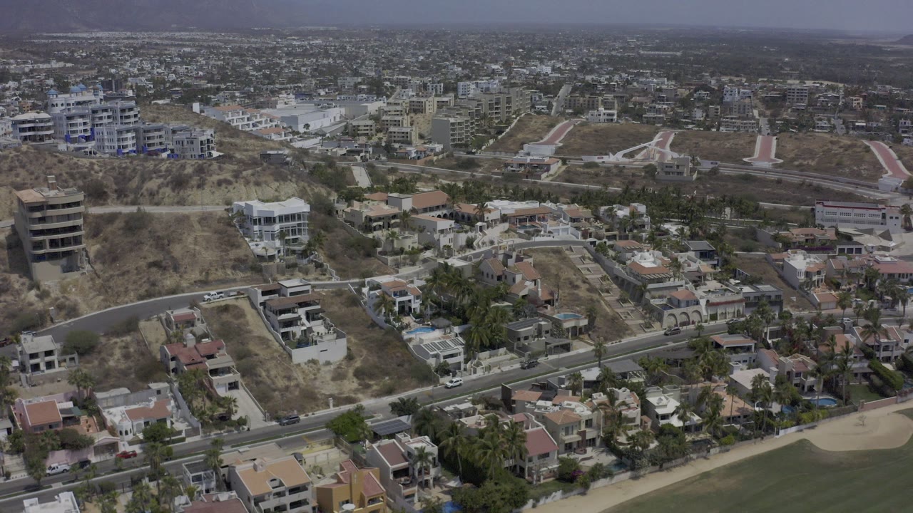 Aerial view of hillside homes, roads, and city blocks under hazy sky.