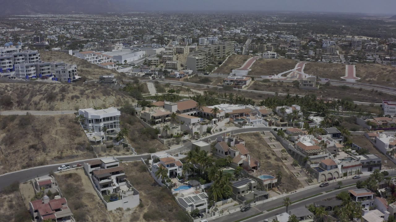 Hillside residential area with modern homes, pools, and city buildings beyond.