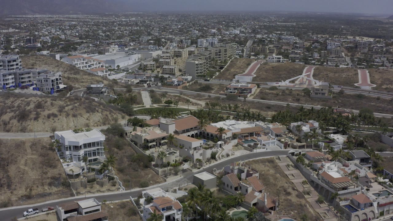 Drone view over hillside homes, roads, and a broad city background.