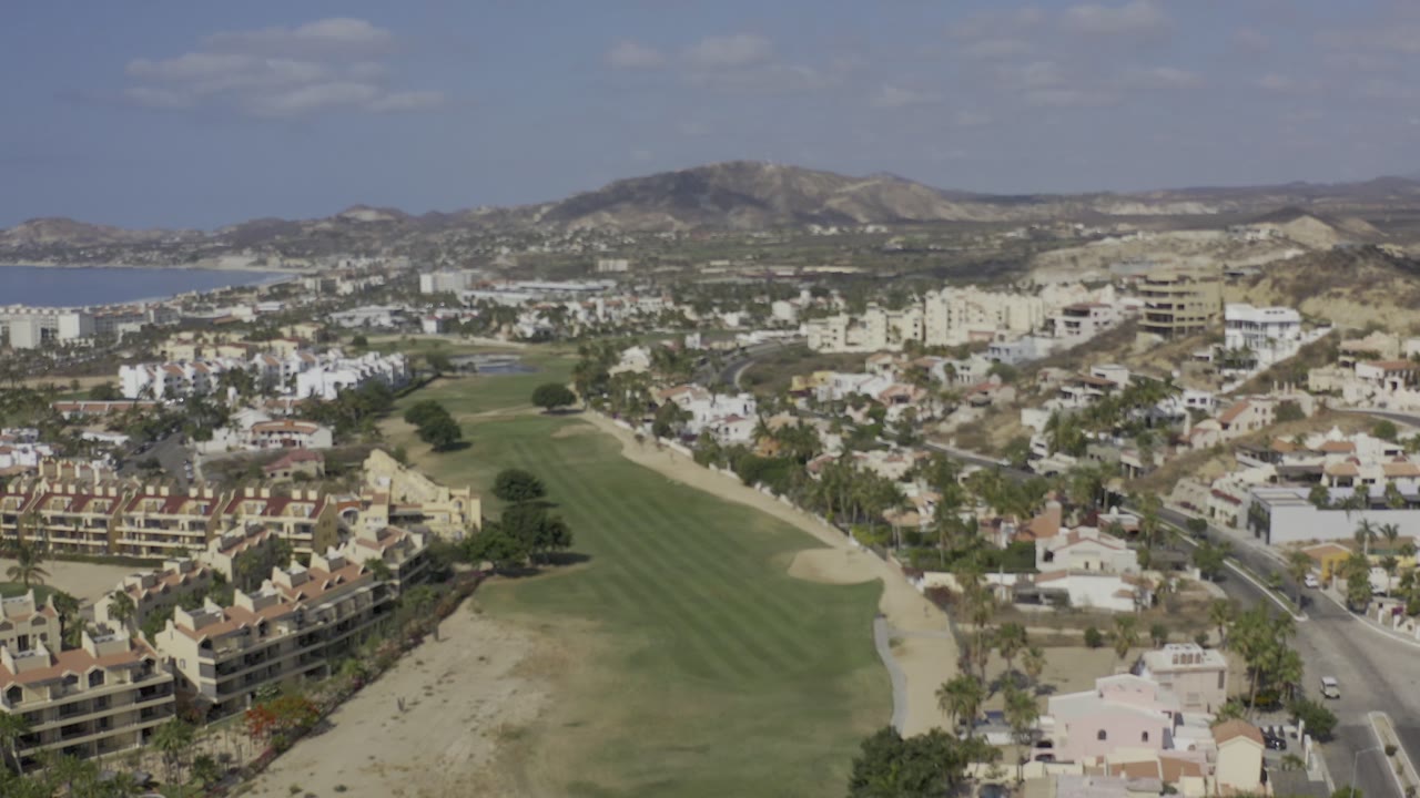 Aerial view over a golf course, homes, hills, and distant water.