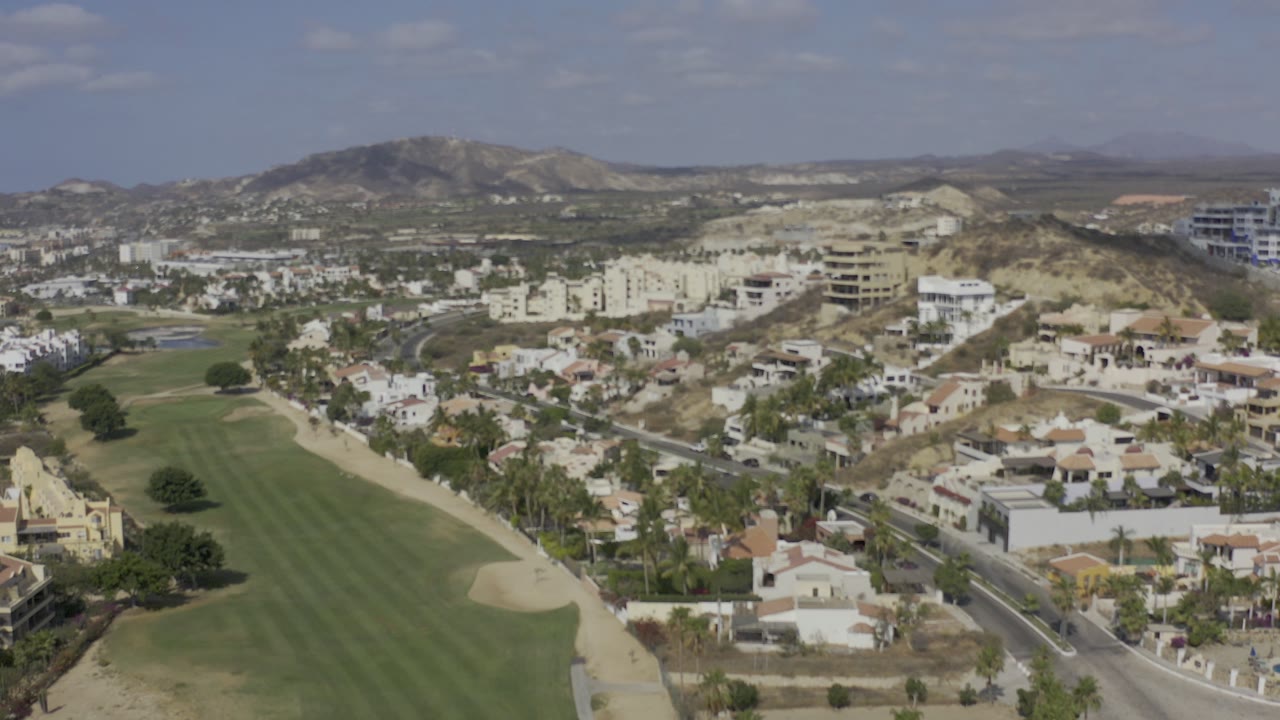 Aerial view of a golf fairway, hillside buildings, roads, and mountains.