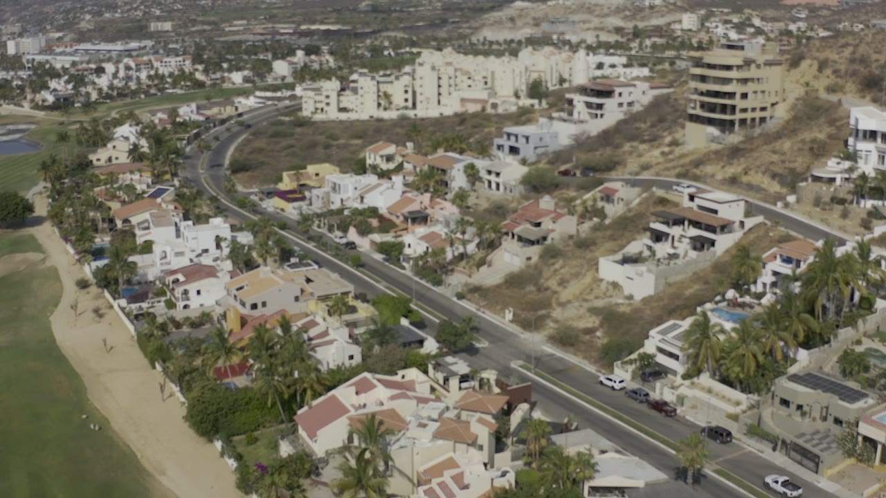 Aerial view of a diagonal road through hillside homes and palms.