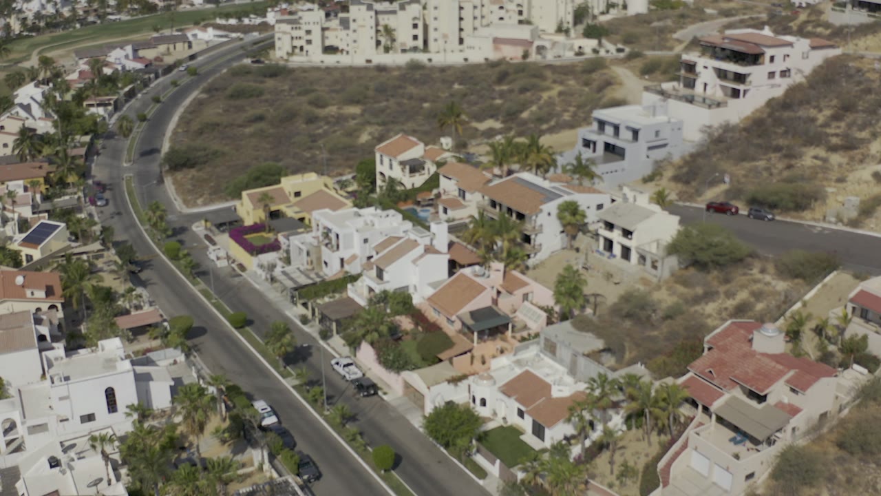 Aerial view of white stucco houses beside a curving road and dry lots.