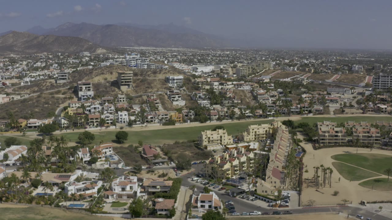 Aerial view of a golf course running through homes and hillside buildings.