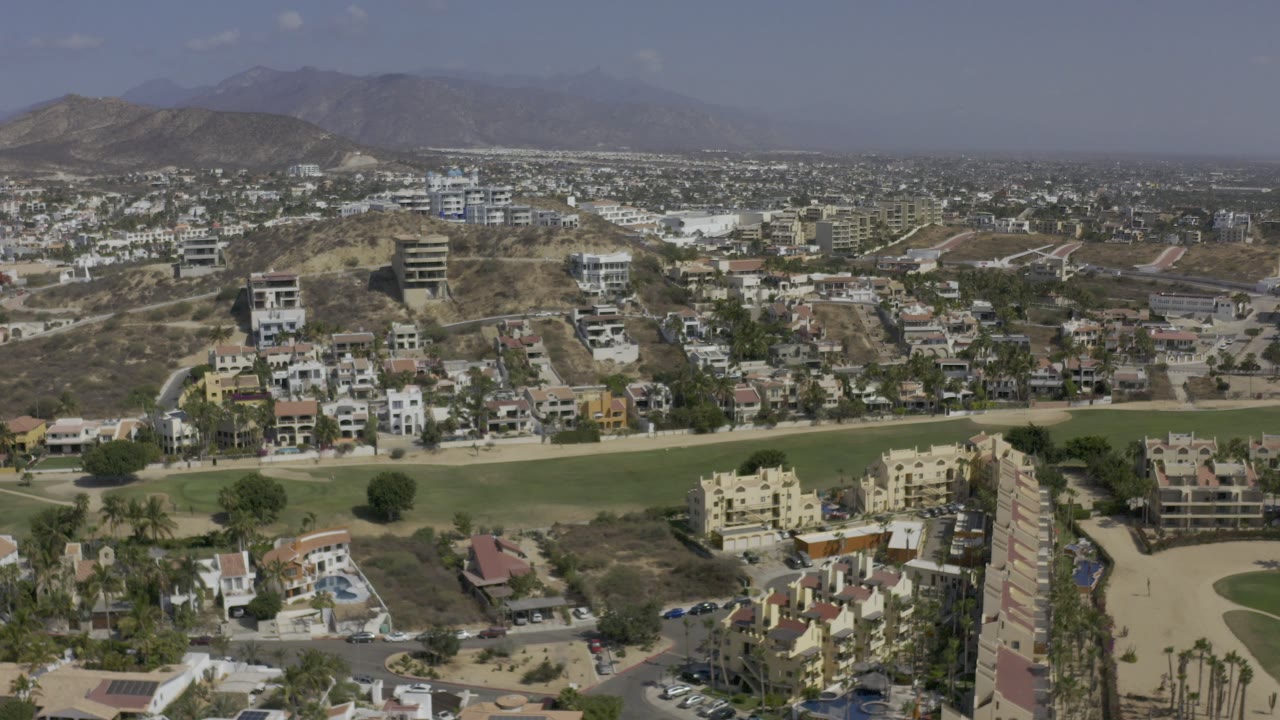Aerial view of residential buildings, streets, grass, and dry hills.