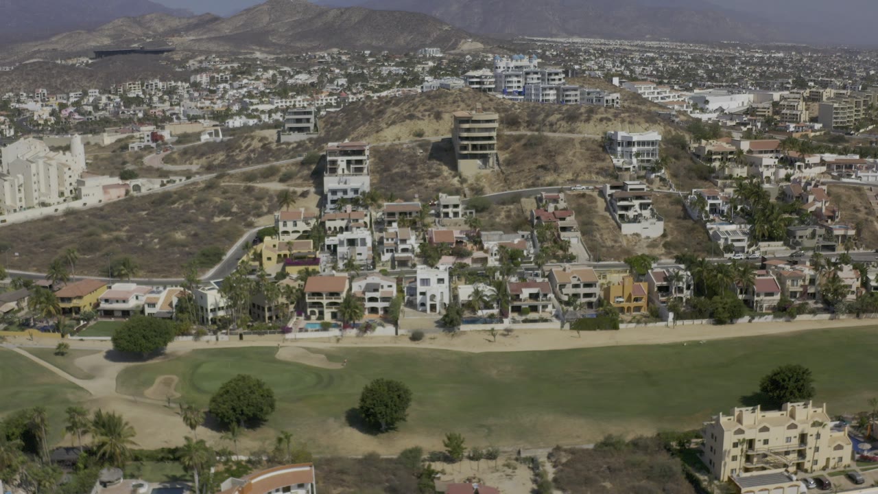 Aerial view of homes above a green field and dry hillside.
