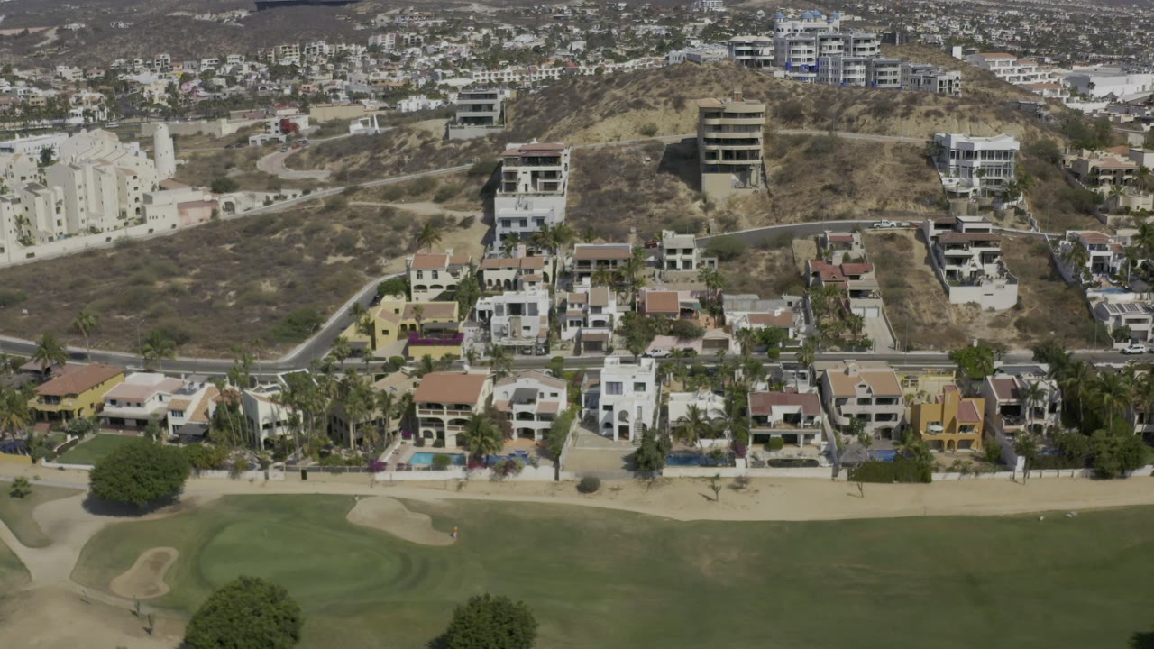 Drone view of homes, roads, and dry hillside above golf greens.