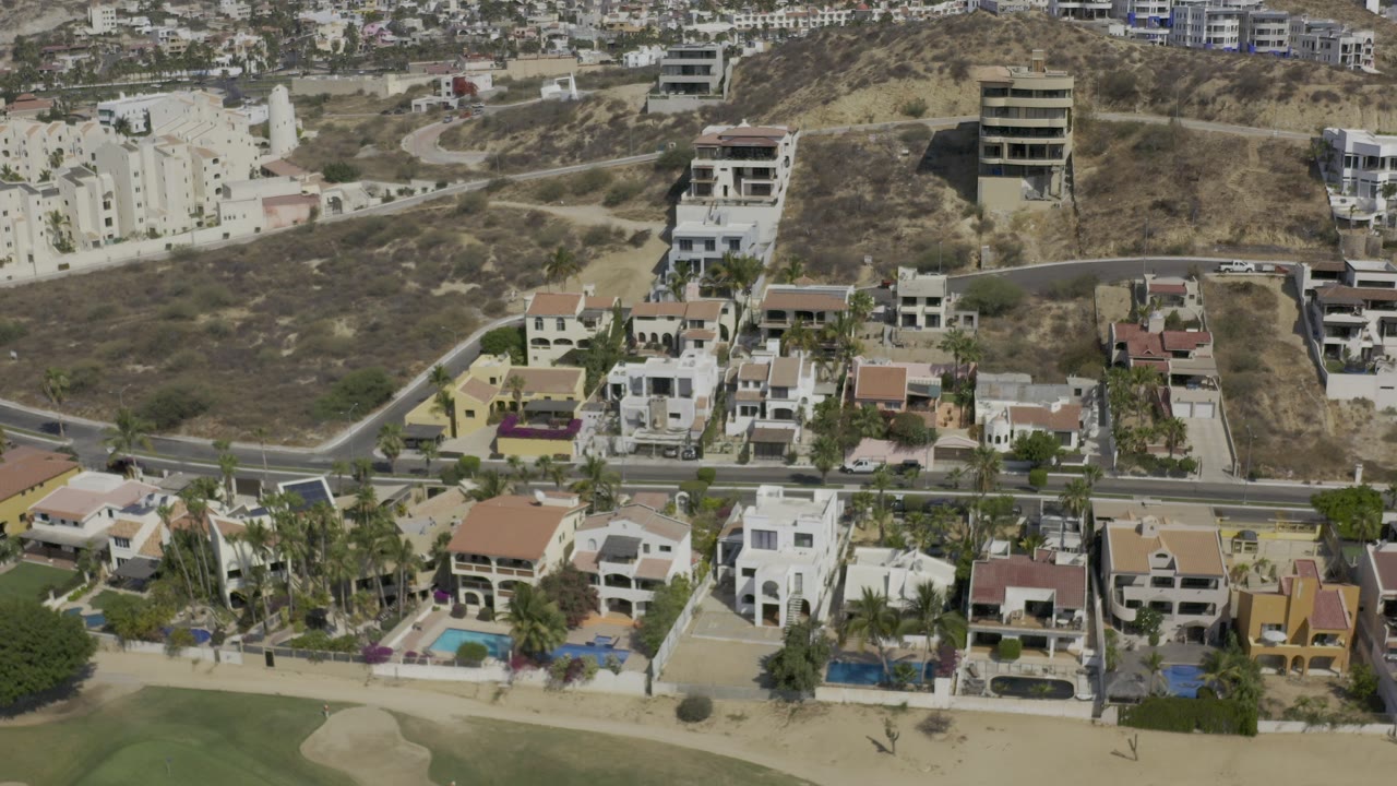 Aerial view of hillside houses, pools, road, and dry terrain.