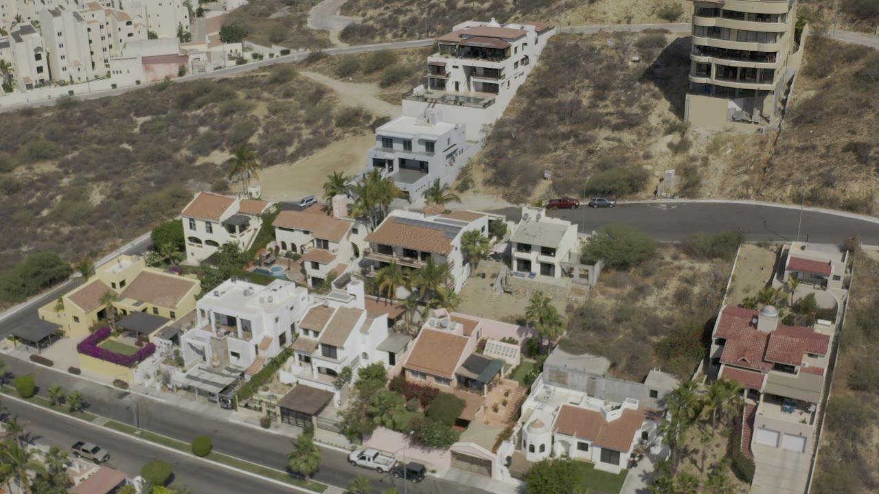 Aerial view of hillside homes, roads, palms, and dry brown terrain.