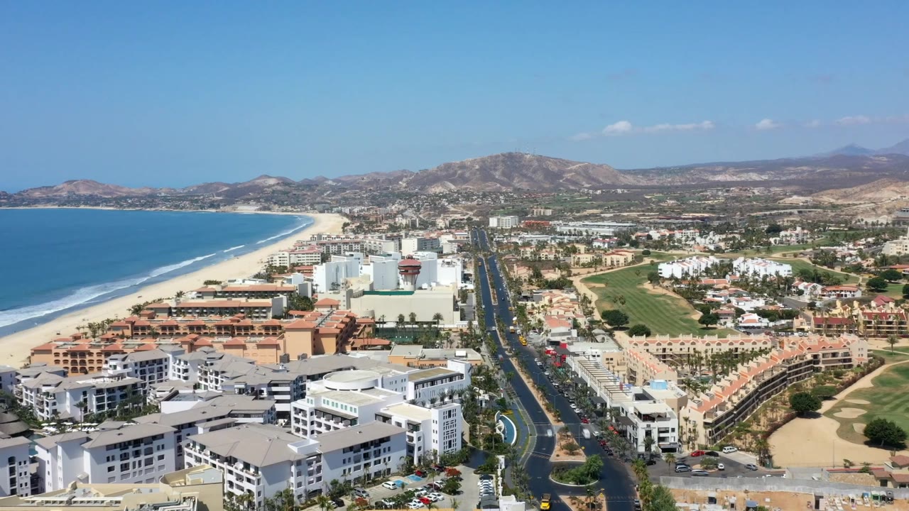 Aerial coastal city view with road, beach, and green grounds