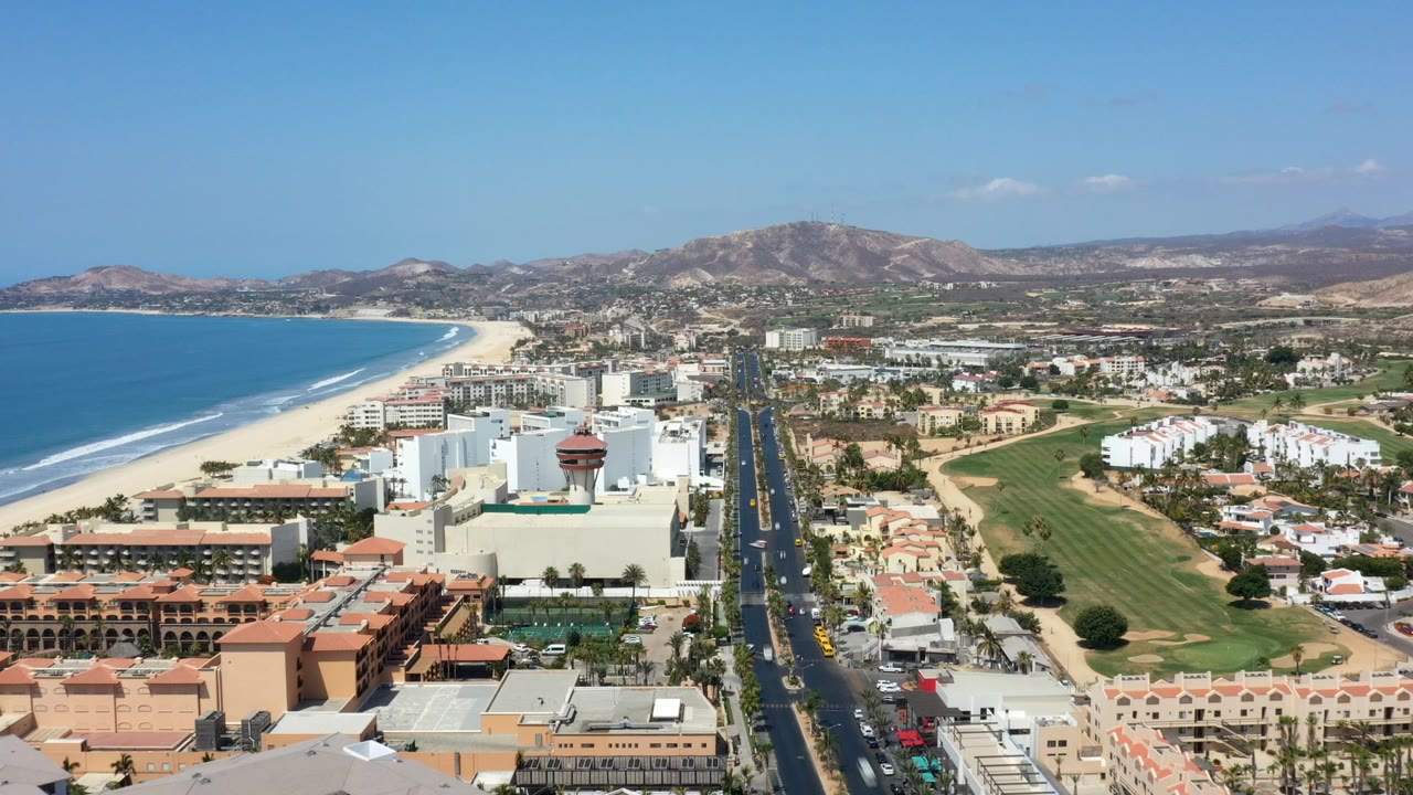 Aerial view of beach, coastal city, road, golf course, and mountains.