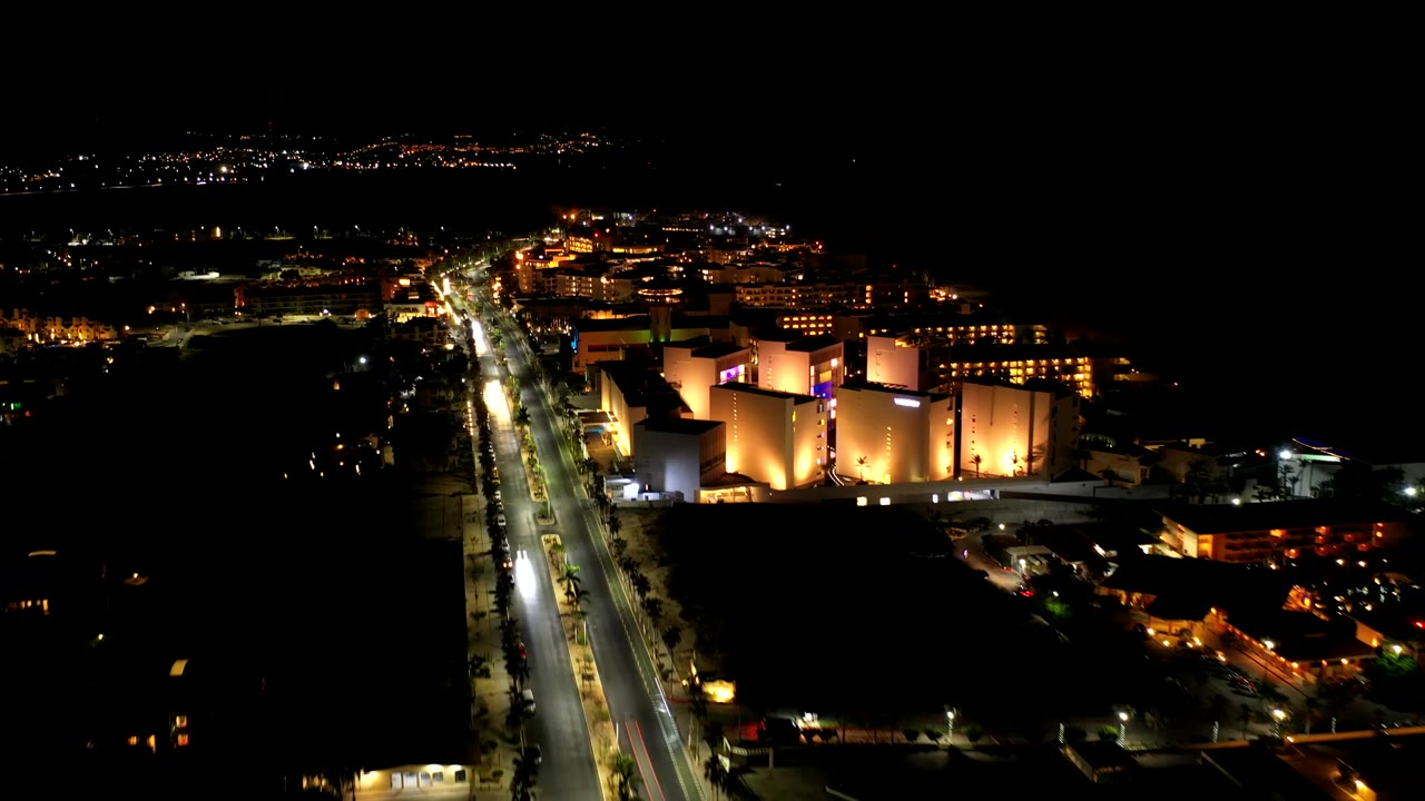 Elevated night view of a road leading past illuminated buildings.
