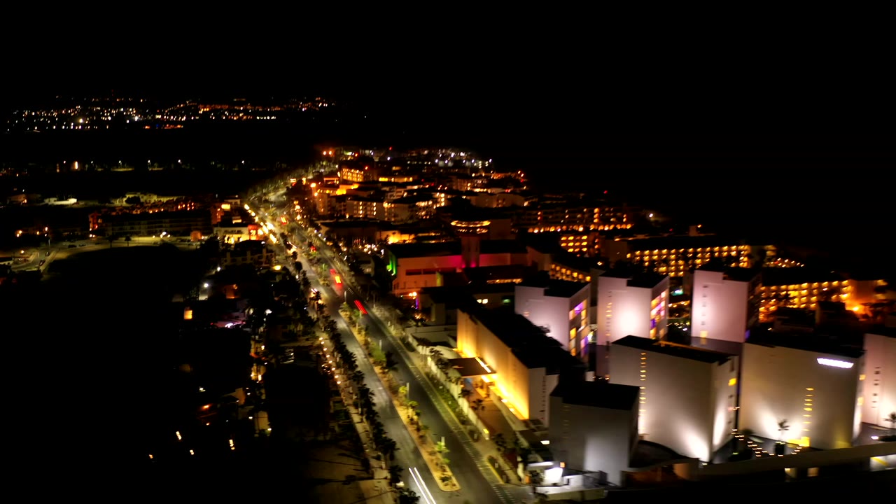 Night aerial view over Los Cabos, Mexico, with a bright road running through modern buildings and no visible people.