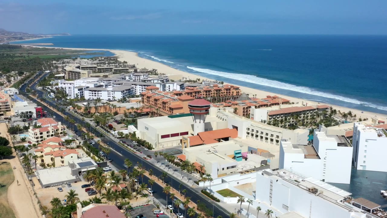 Aerial coastal city view with buildings, beach, ocean, and distant hills.