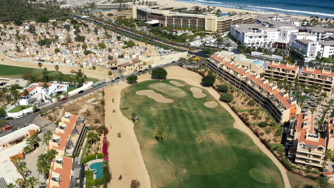 Aerial view of a golf course beside resort buildings and the coast.