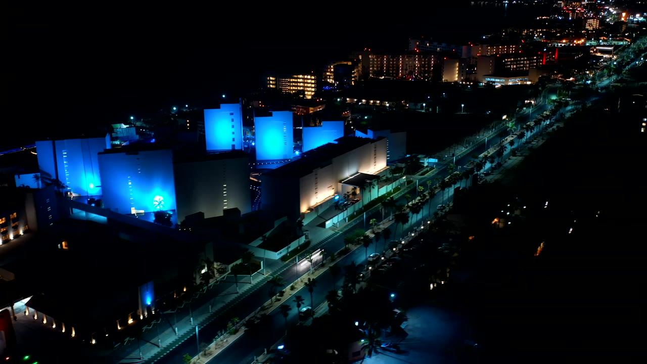 At 0:00, a Los Cabos night aerial looks over blue-lit modern buildings, a dark road, distant window lights, and no visible people.