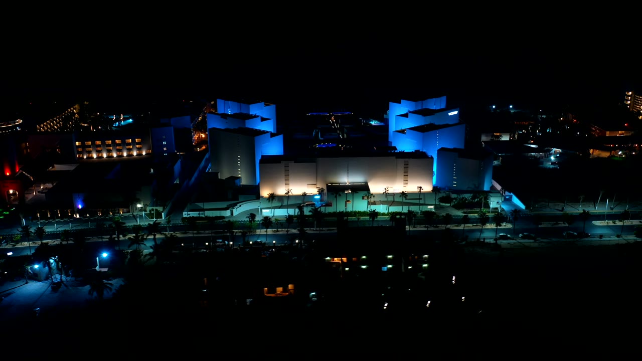 Night aerial view of a blue-lit modern building complex and dark streets.