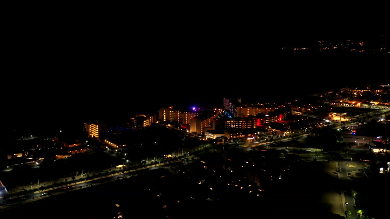 Night bird's-eye view in Los Cabos with the building cluster centered, scattered road lights below, and no visible people.