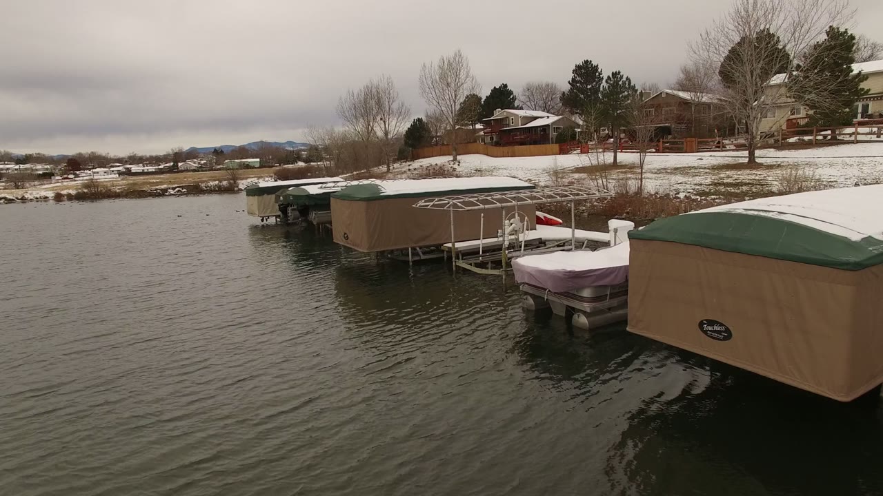 Snowy dock area with covered boats beside rippled lake water.