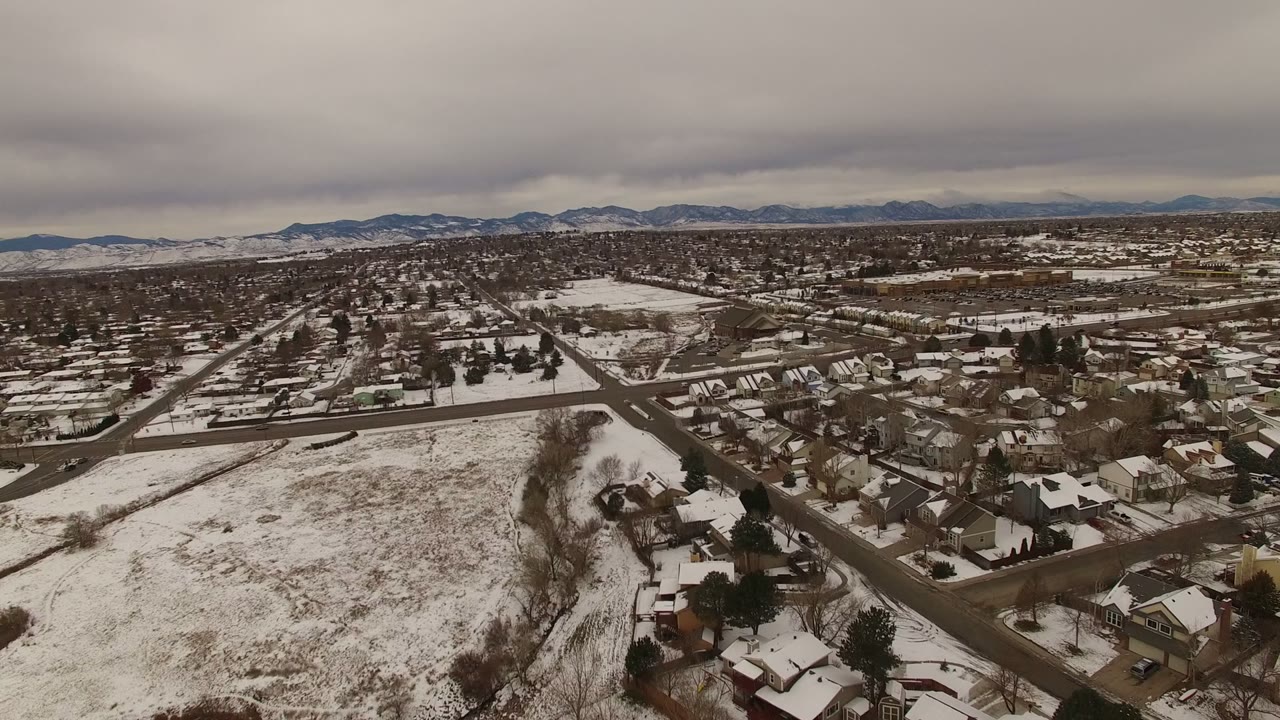 Second aerial frame from Jefferson, Colorado with the snowy field still prominent, houses clustered to the right, distant foothills, and no visible people.