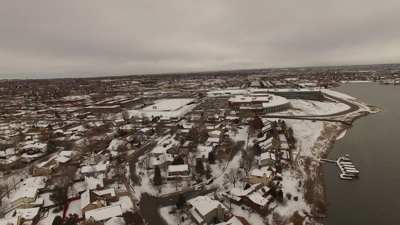 Snowy residential neighborhood beside a narrow body of water under gray clouds.
