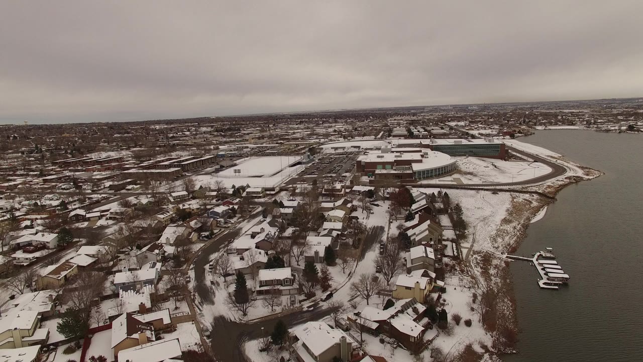 Aerial view of snowy lakefront houses beside dark water.