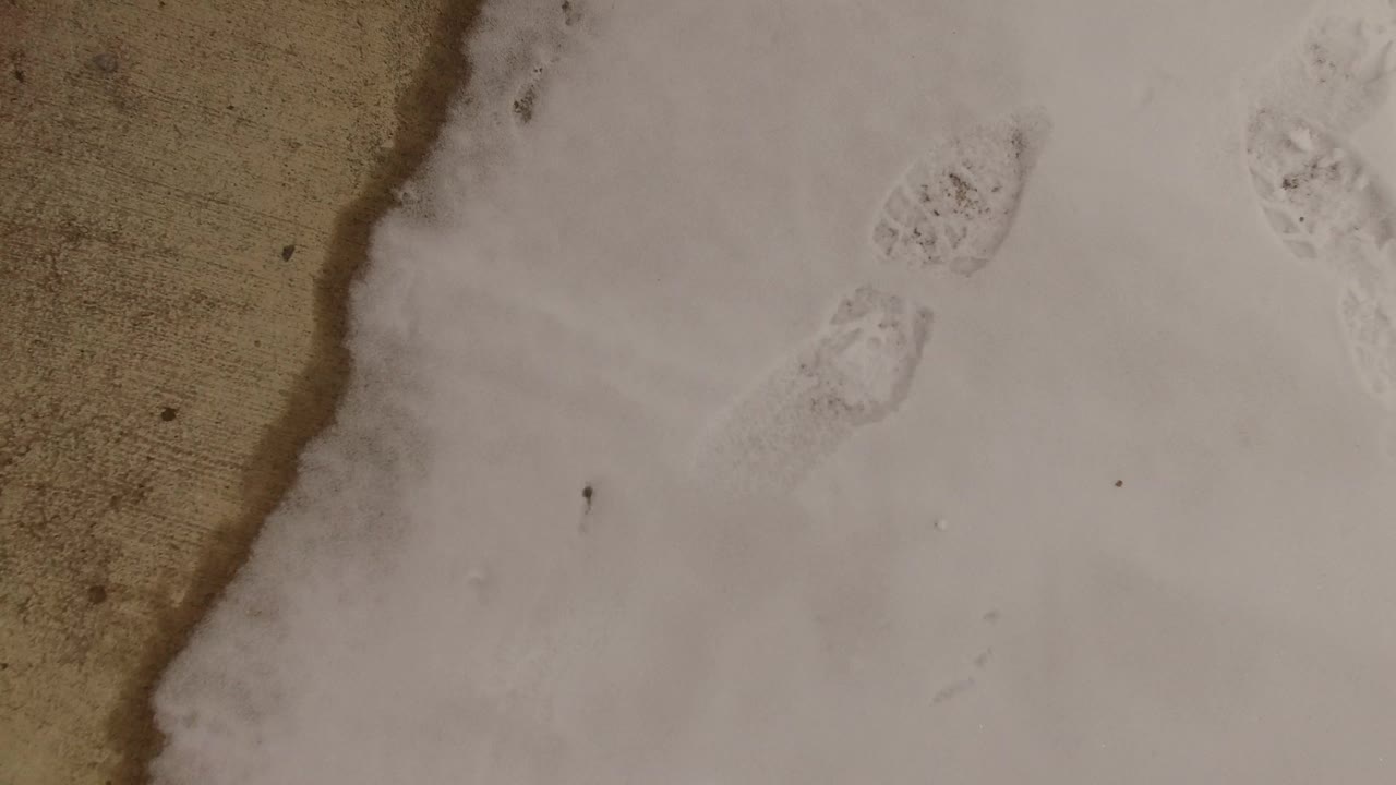Snow field with a curved tan ground edge and faint footprints.