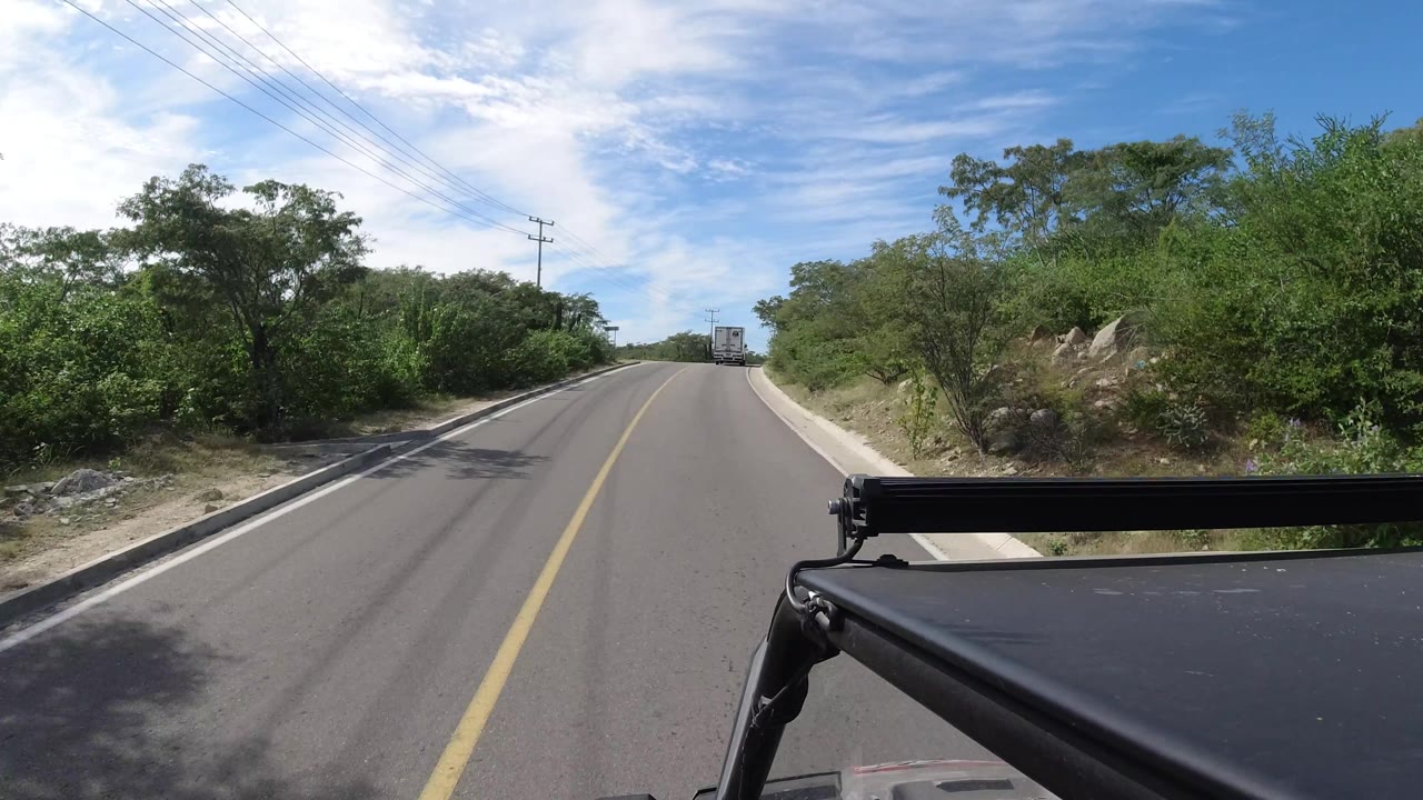 Vehicle POV on a curving road with trees, rocks, and brush along the shoulder.