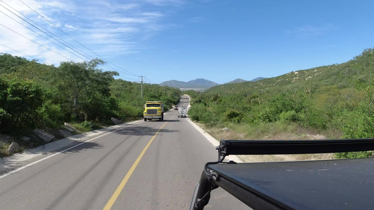 Two-lane road with a yellow truck ahead and green hills on both sides.