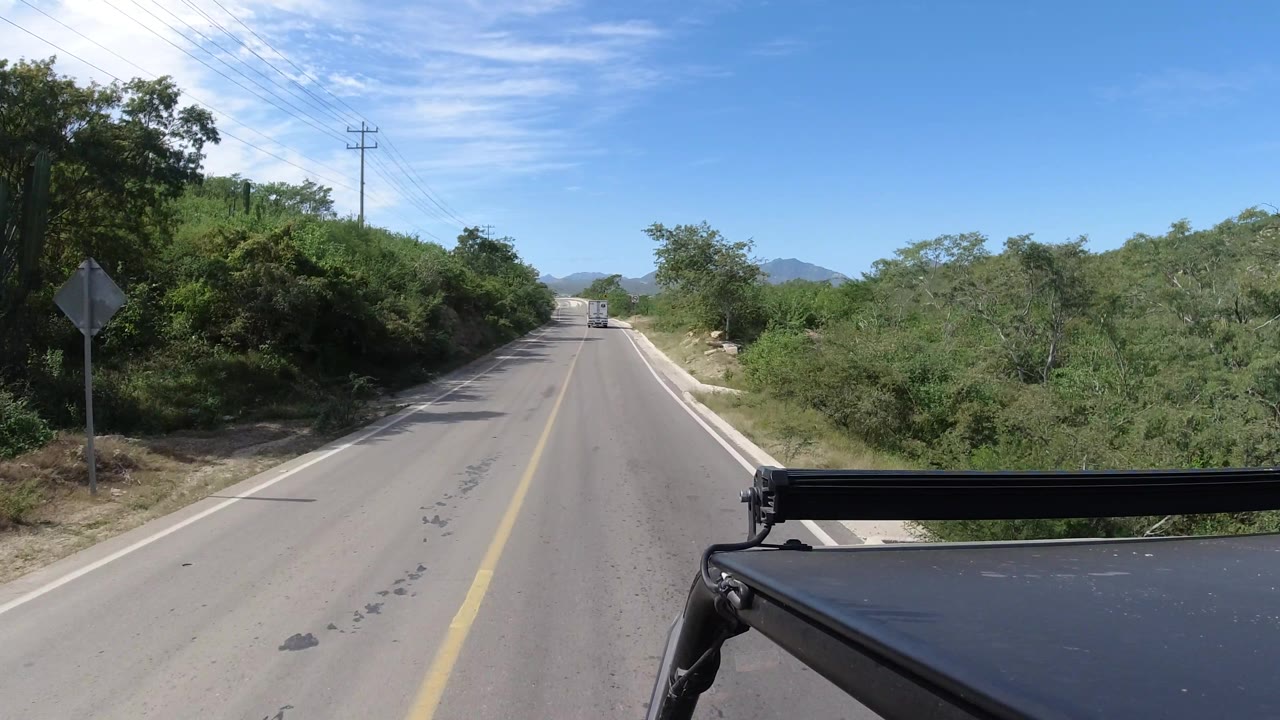 Rural road with sign, shrubs, and distant hills
