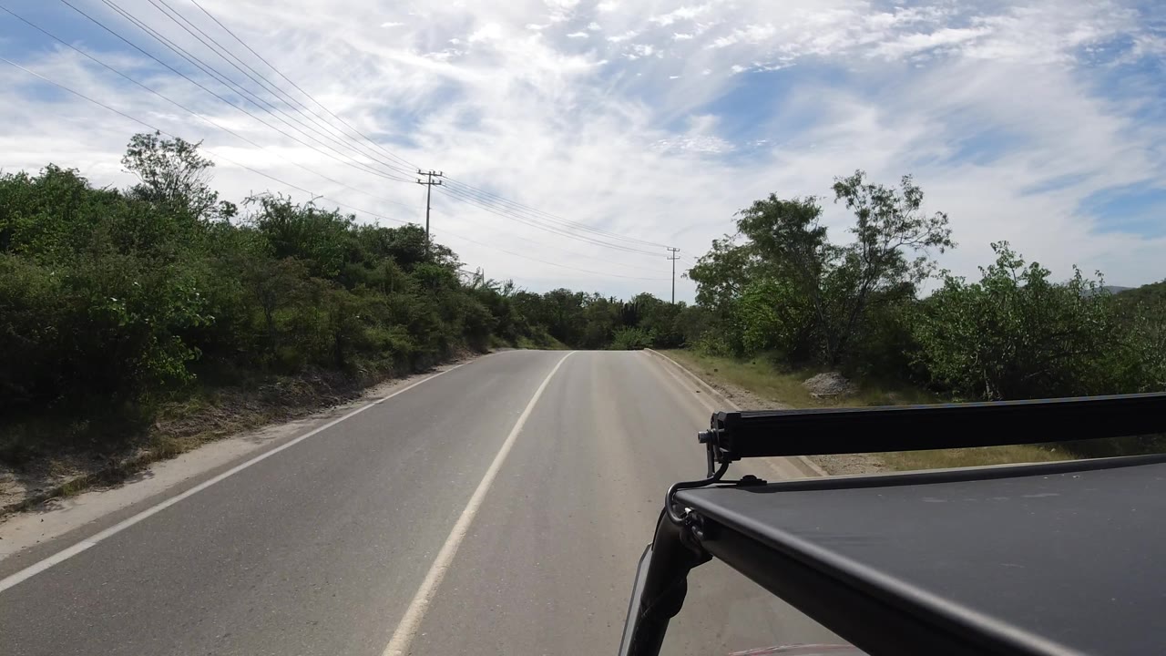 Road beginning to curve with brush and low hills ahead.