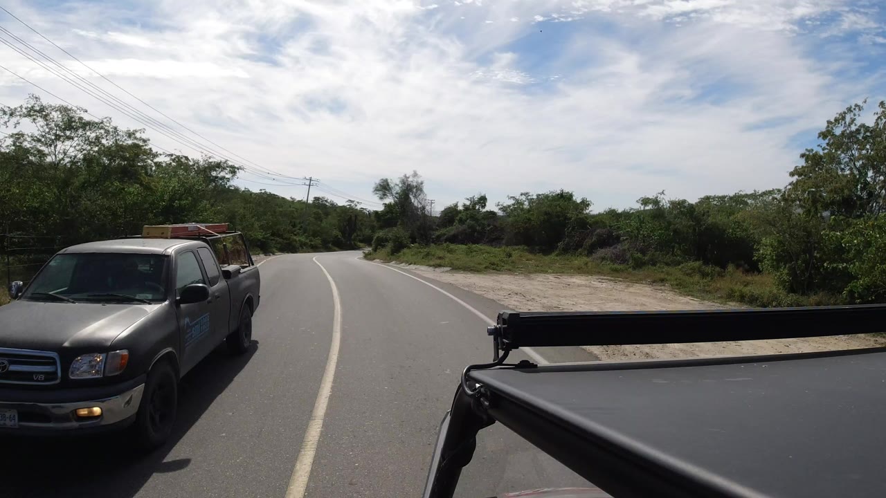 Pickup truck beside a curving road with roadside trees and cloudy blue sky.